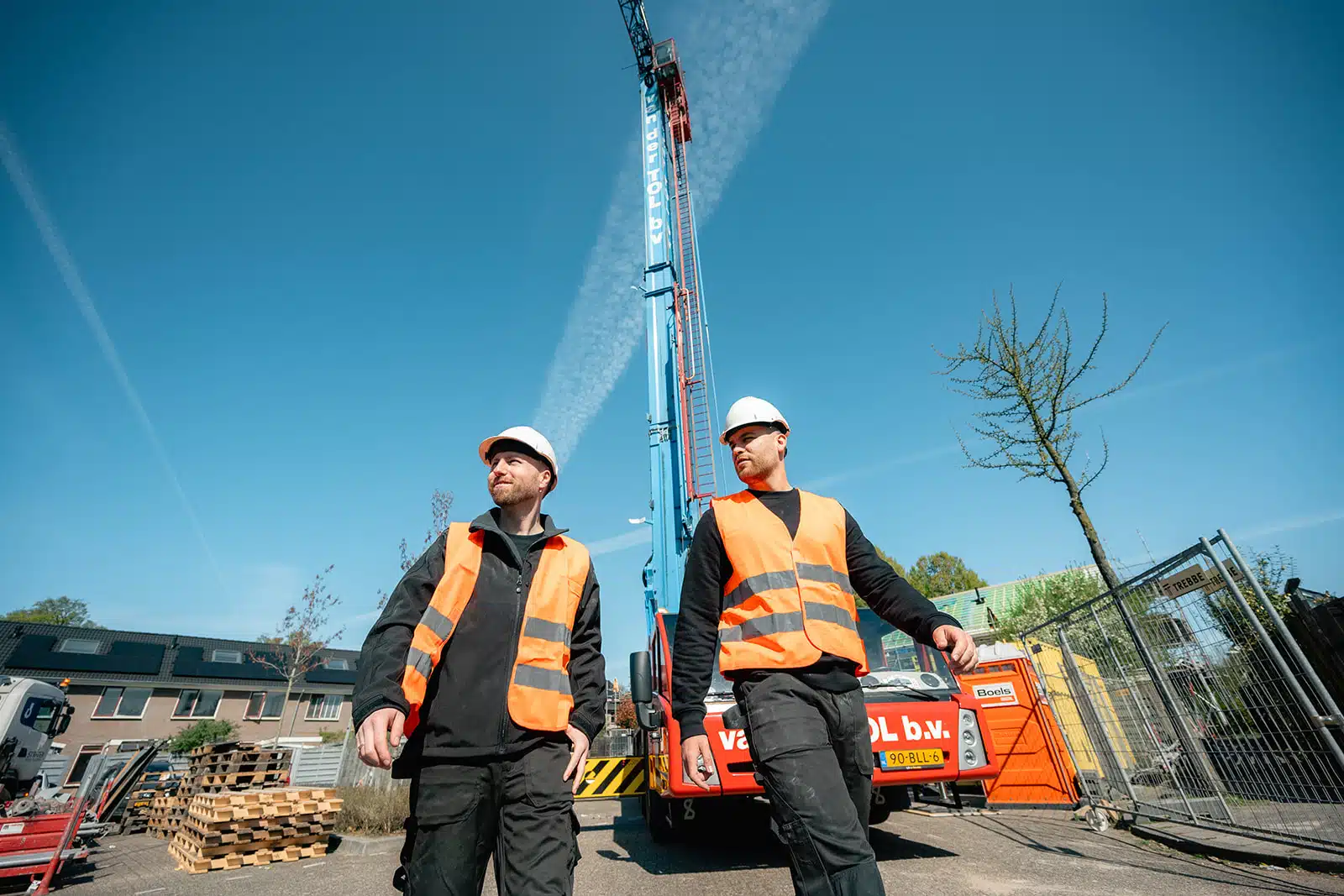 Twee medewerkers in oranje hesjes bij hijskraan